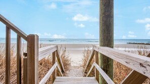 Une promenade en bois qui mène à une plage d’où l’on a une vue dégagée sur l’océan.