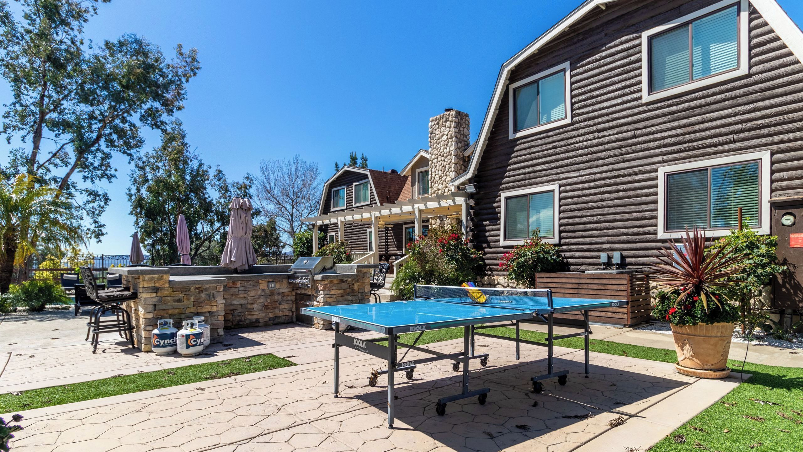 Une cabane en rondins dotée d’un patio comprenant une table de ping-pong, des sièges d’extérieur et une cheminée en pierre.