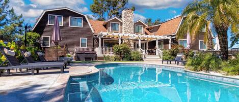 A large house with a swimming pool, a covered patio, and a stone chimney.