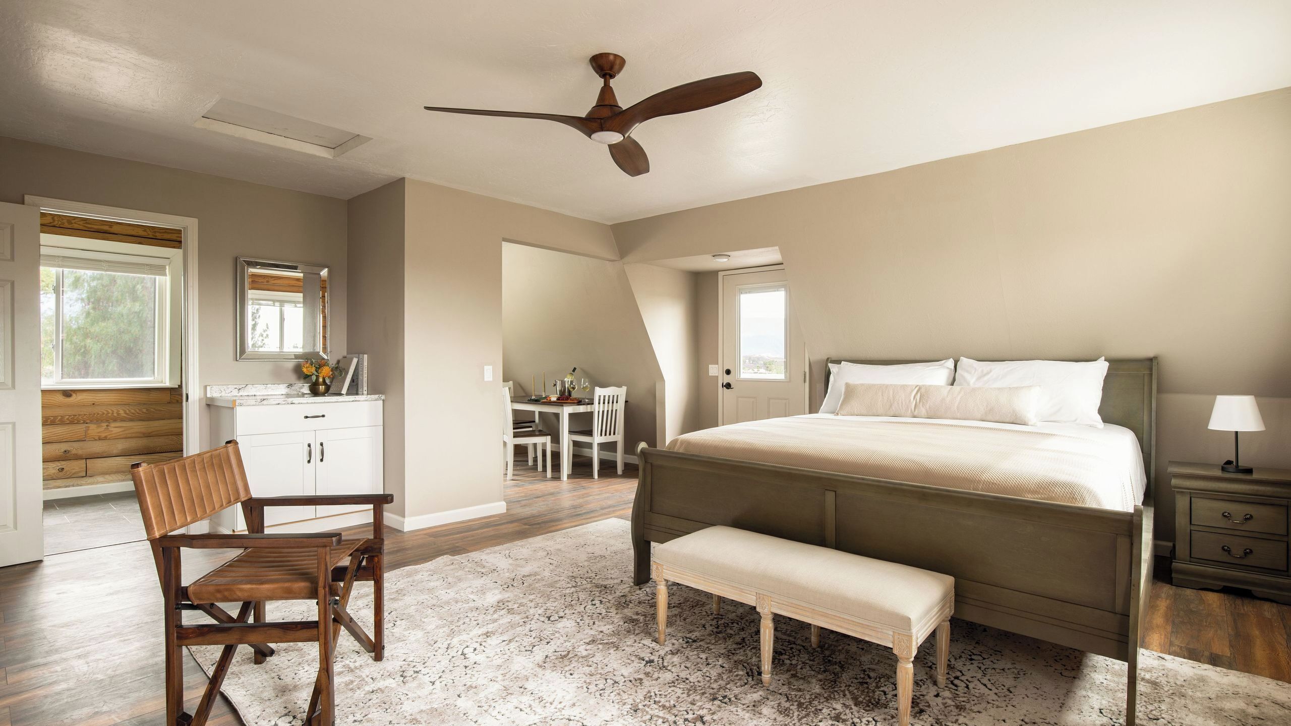 A bedroom with a bed, a desk, a chair, a ceiling fan, and a window.