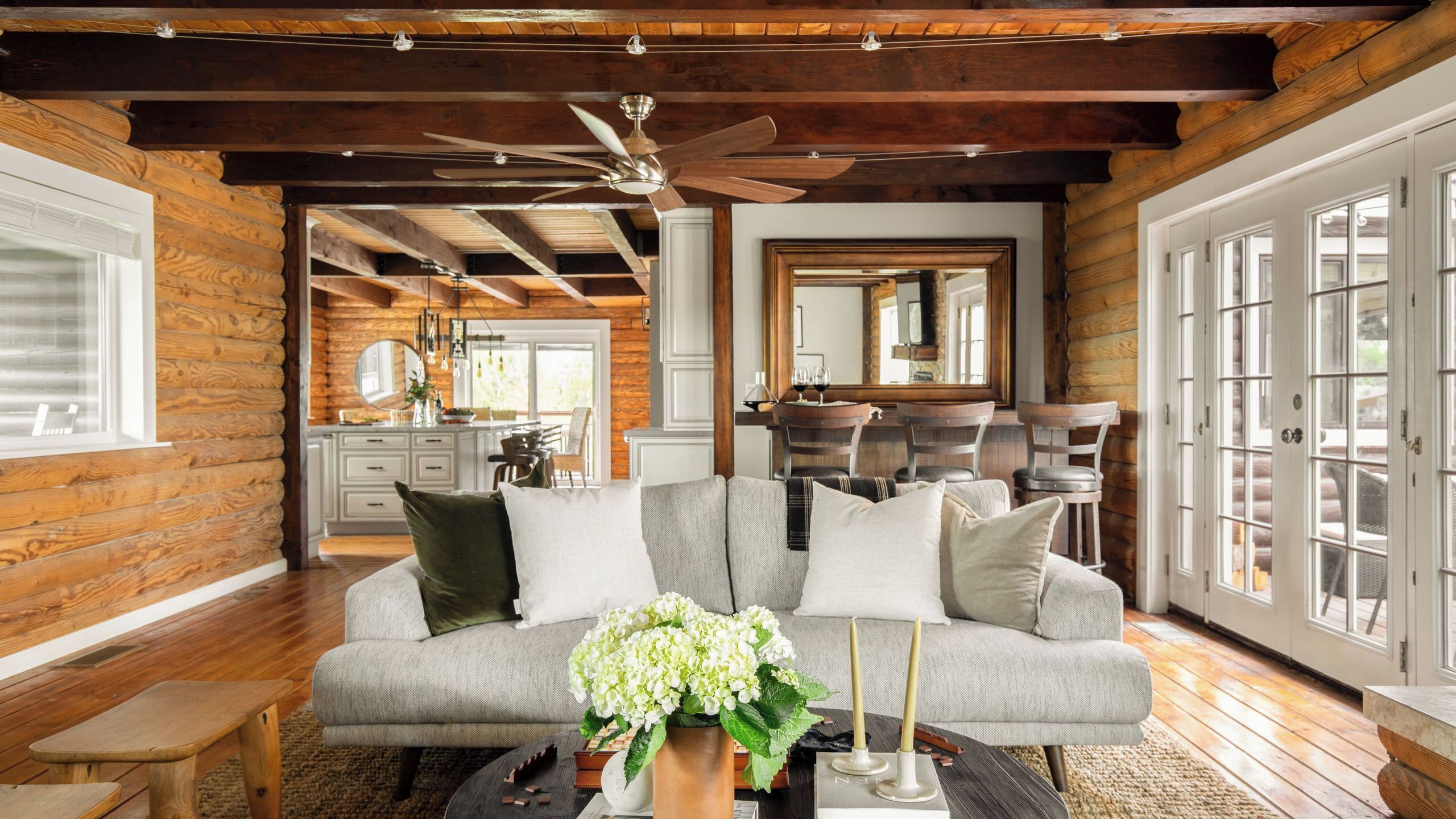 A log cabin interior with a sofa, dining area, and large windows.
