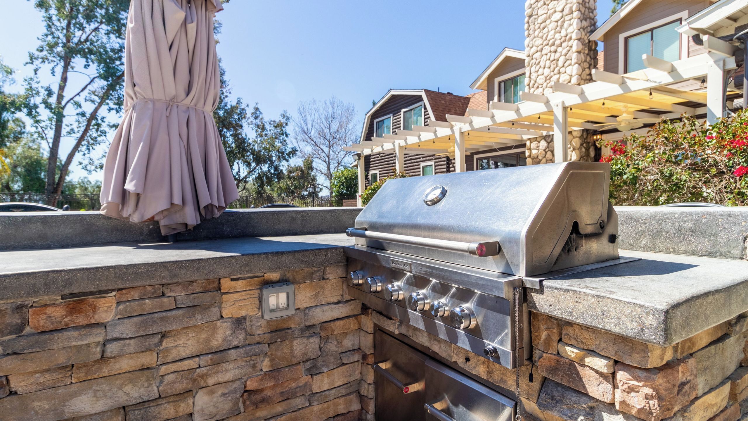 Une cuisine extérieure dotée d’un barbecue intégré, d’un mur en pierre et d’un patio couvert.