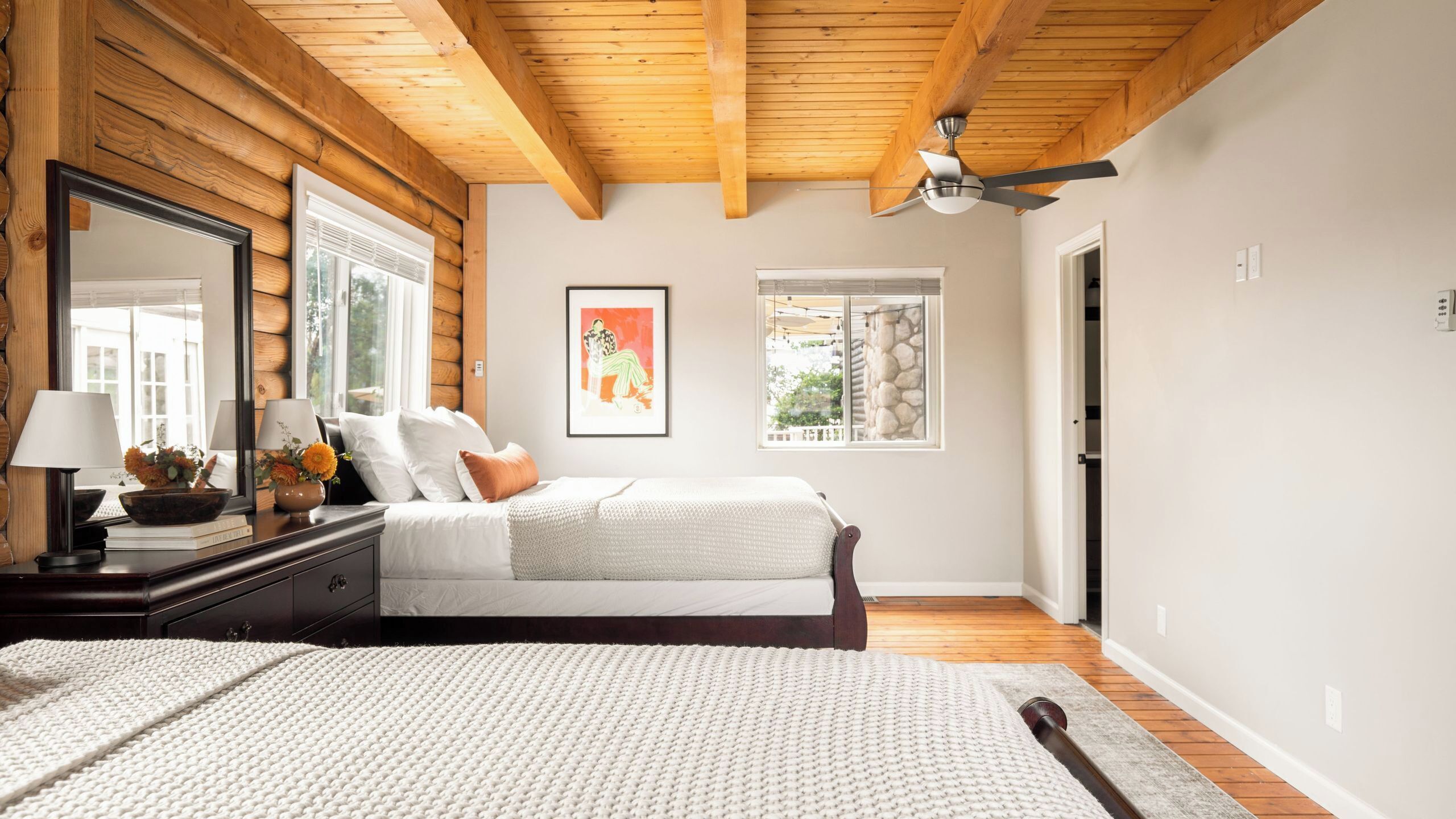 Une chambre avec un plafond en bois, un lit avec une literie blanche, une table de chevet avec une lampe et un grand miroir.