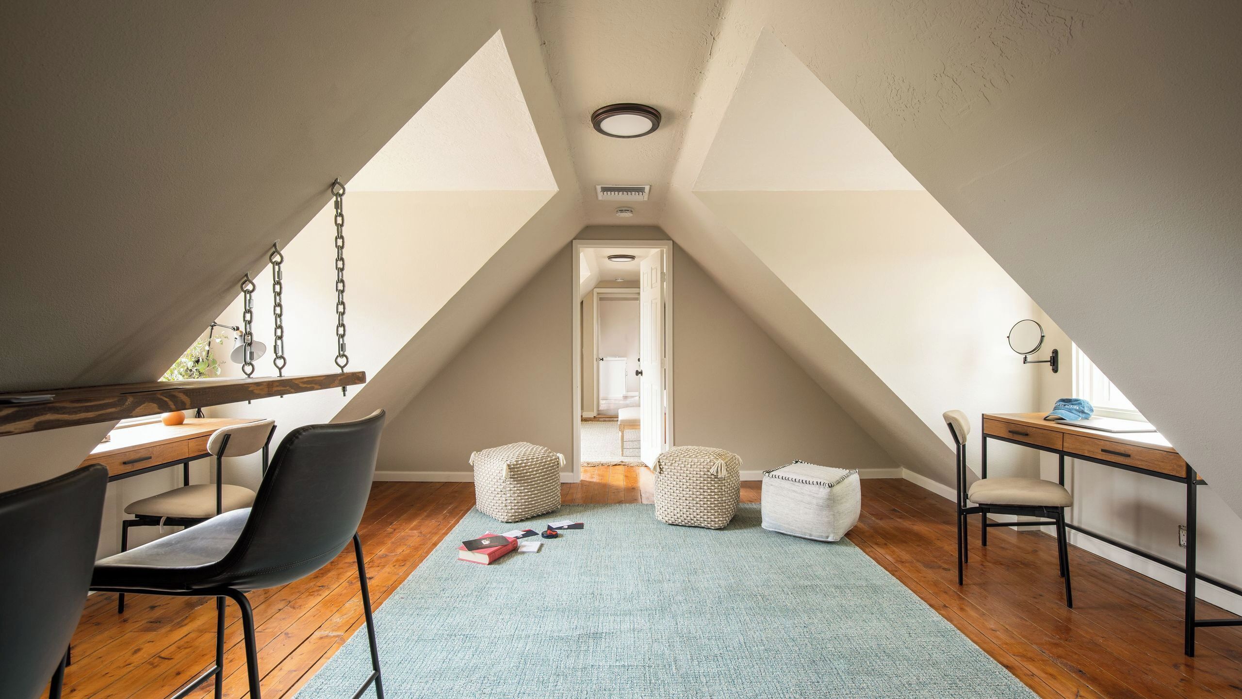 An attic room with a desk, chairs, a swing, and a view of the adjacent bedroom.