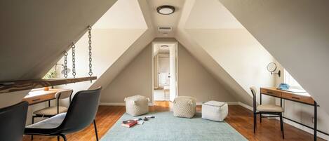 An attic room with a desk, chairs, a swing, and a view of the adjacent bedroom.