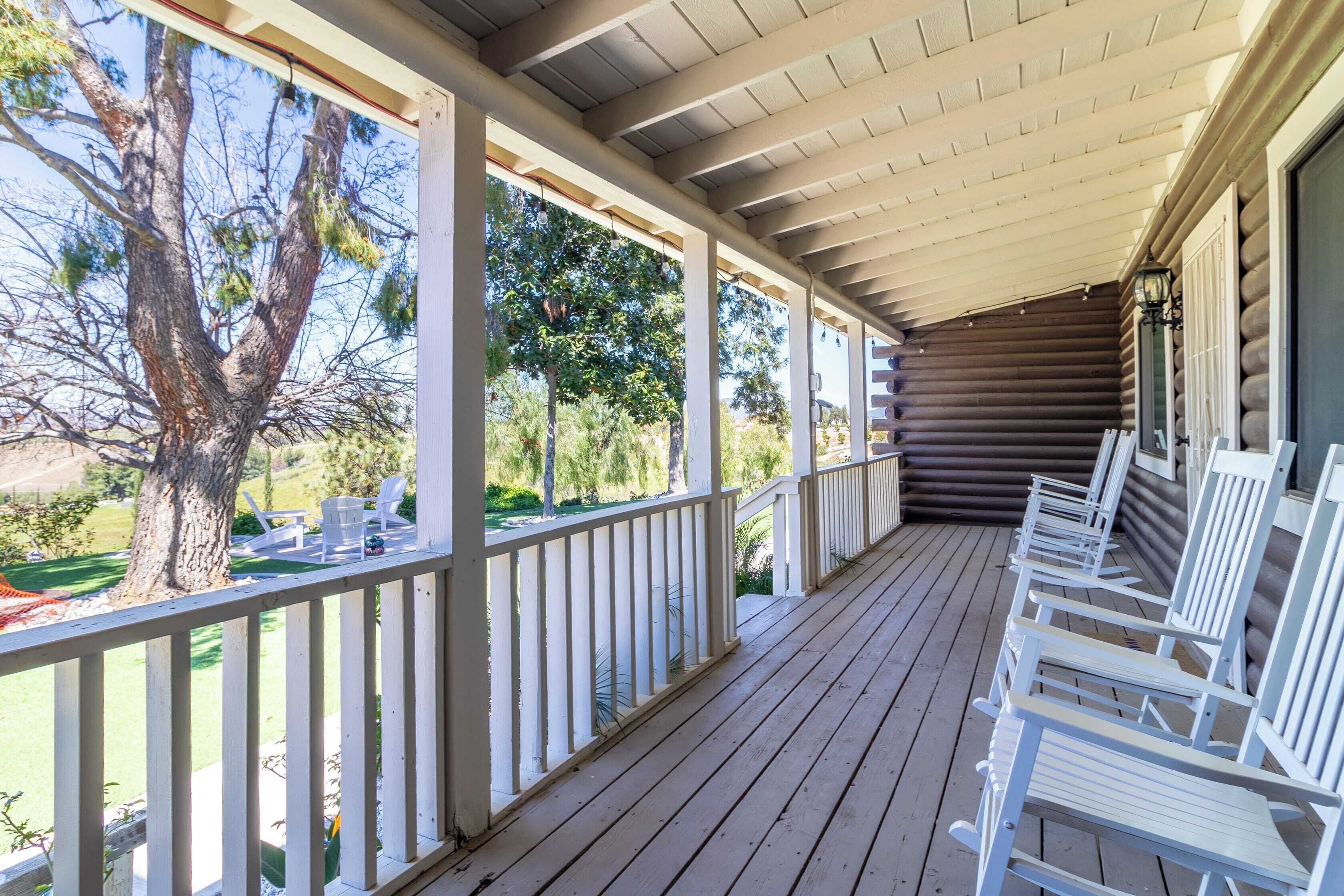 A covered porch with white railings, wooden benches, and a view of a tree and landscape.