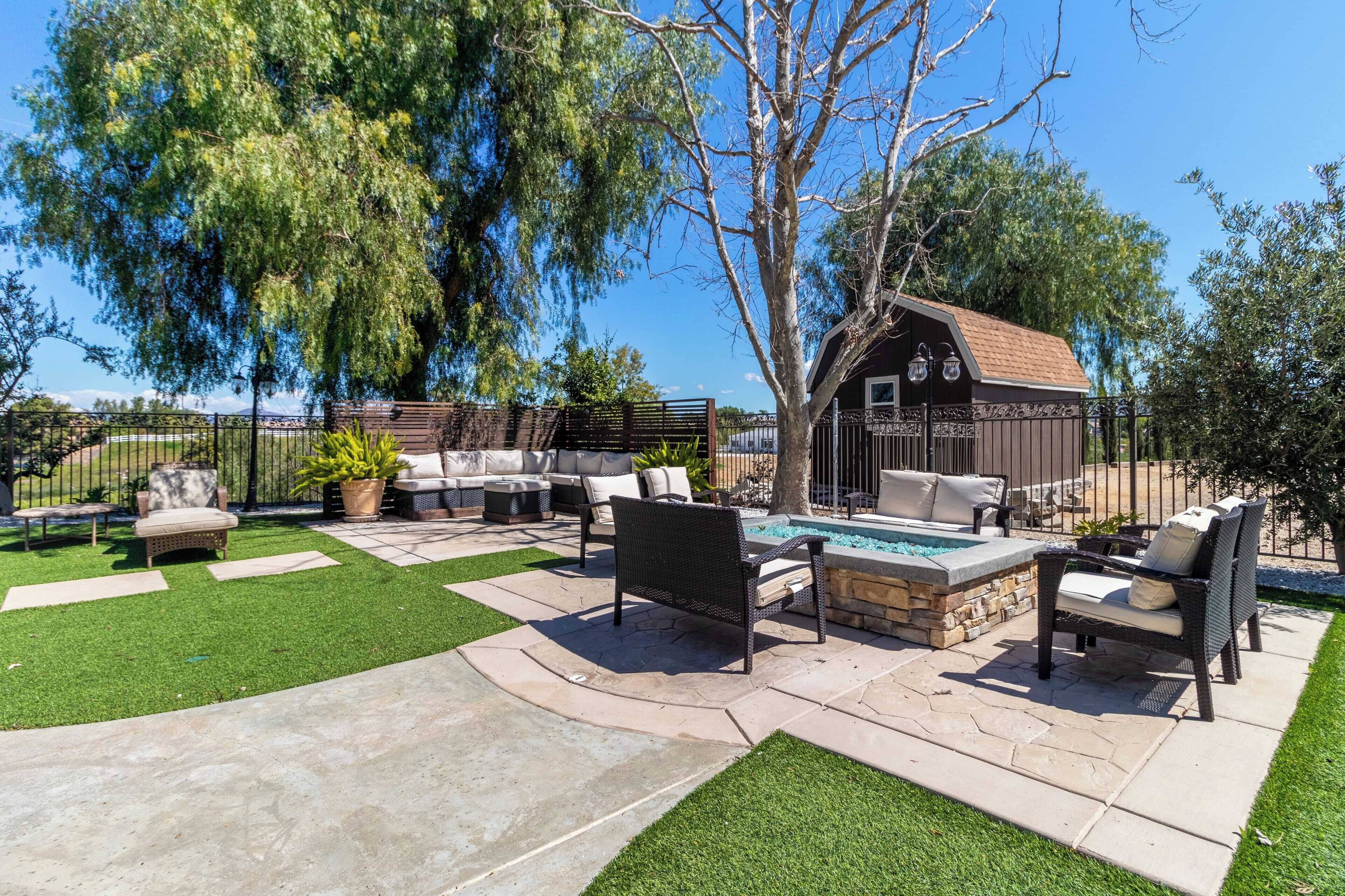 A patio area with outdoor furniture, a stone fire pit, and a small shed.