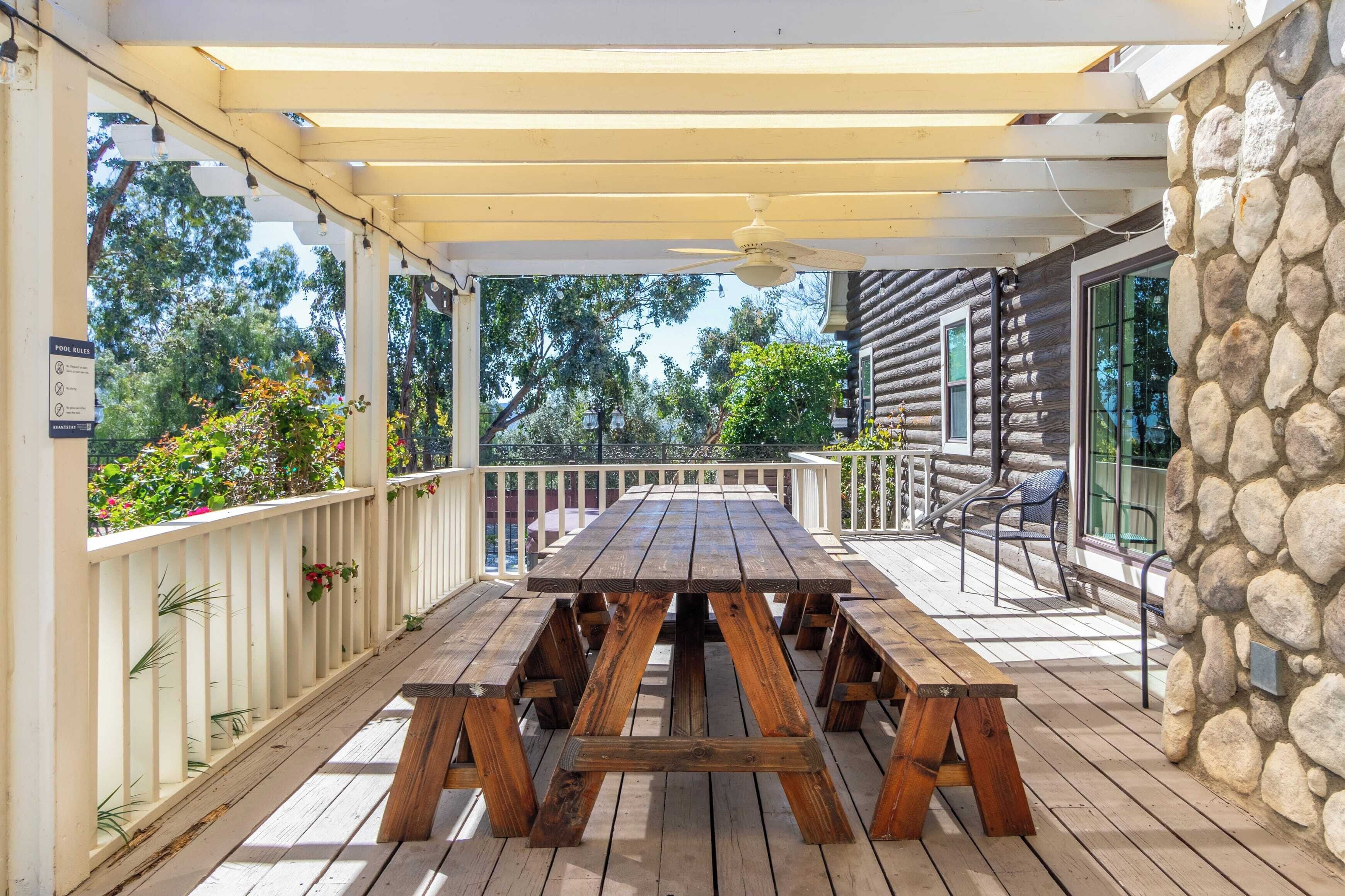 A covered wooden deck with a picnic table and benches, stone wall, and outdoor seating area.