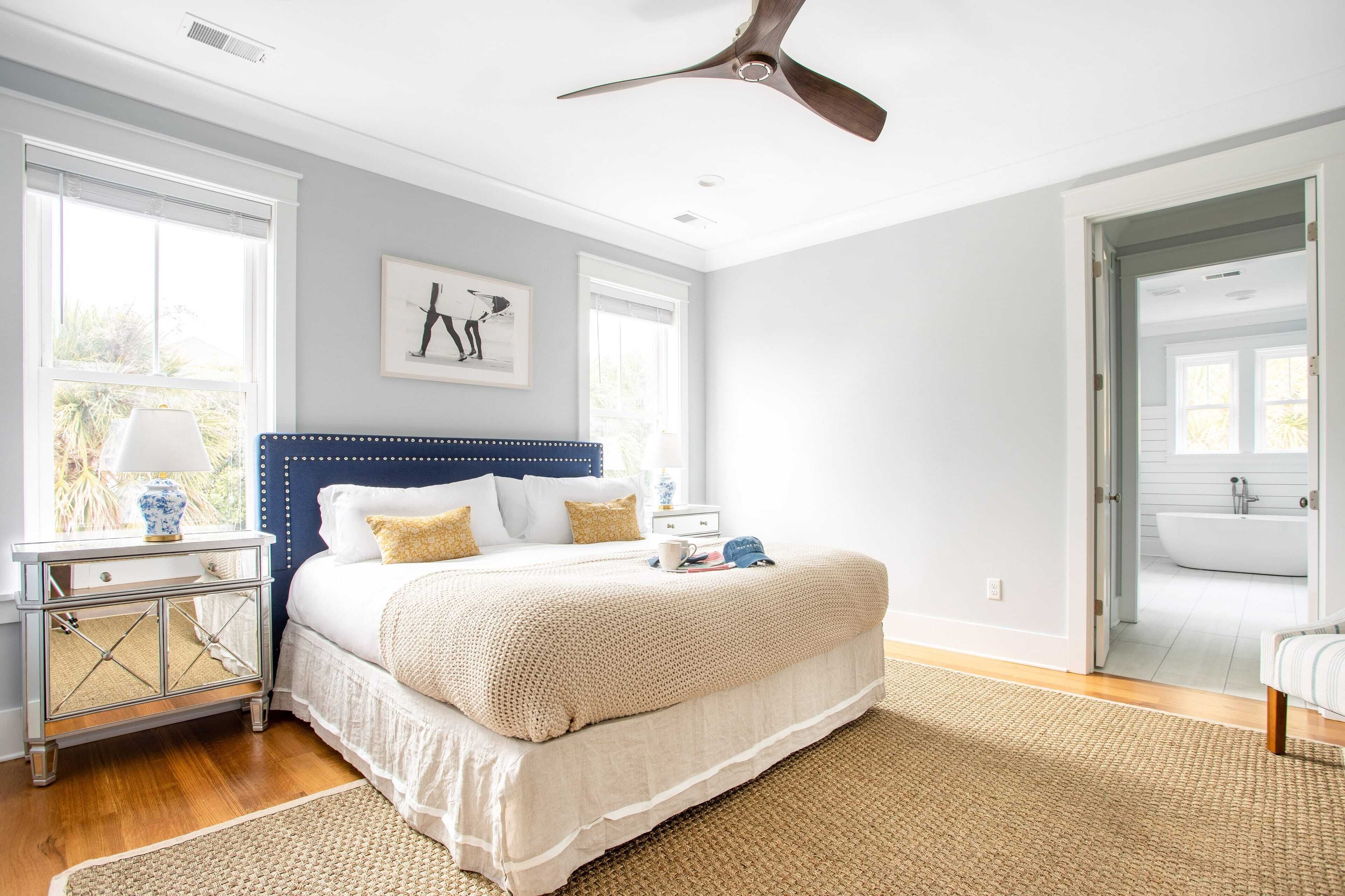 A bedroom with a large bed, a ceiling fan, a nightstand, and a window with blinds.