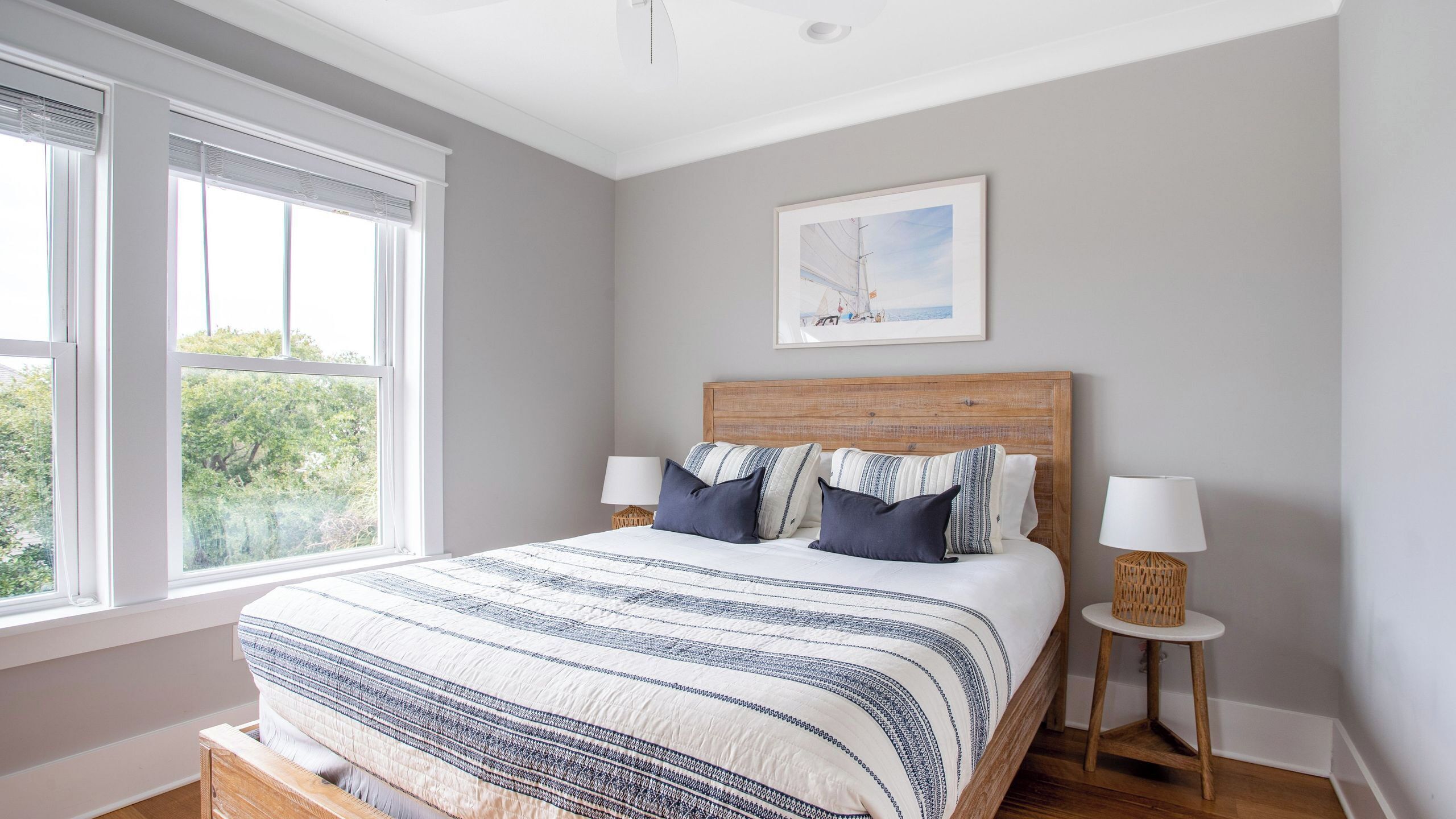 A bedroom with a bed, two bedside tables, a window, and a framed picture on the wall.