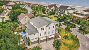 An aerial view of a residential area with houses, a swimming pool, and a beach in the background.
