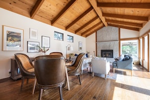 Amplia sala de estar con piso de madera, chimenea y comedor con sillas de cuero.