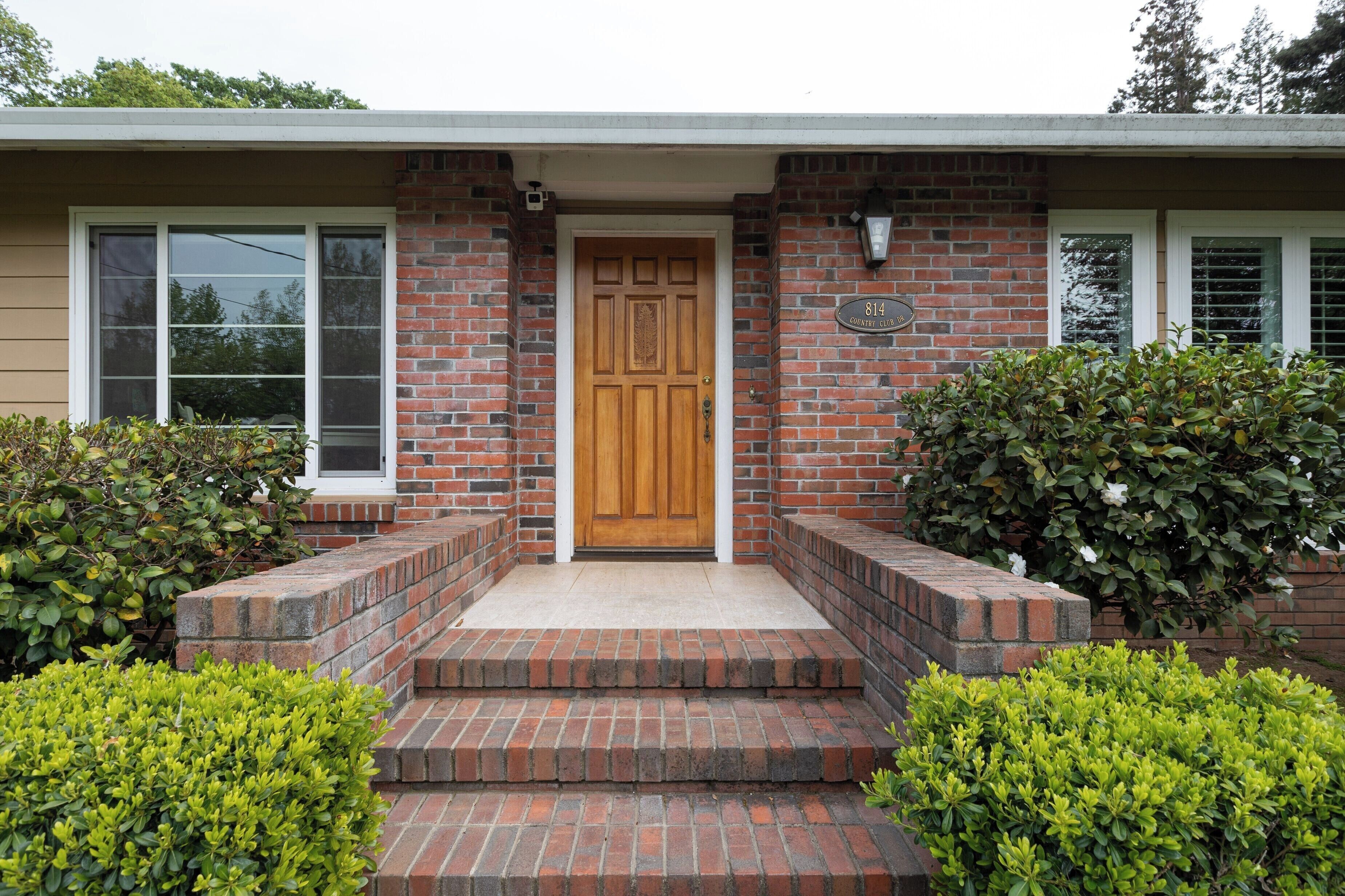 A brick house with a wooden front door, a mailbox, and a number plate.