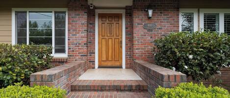 A brick house with a wooden front door, a mailbox, and a number plate.
