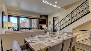A dining area with a wooden table set for six, a sofa, a staircase, and a balcony with a view. - Juniper Landing 3 Bedroom by Avantstay Condo in Park City Mountain Resort w/ Pool, Hot Tub & Gym (Park City)