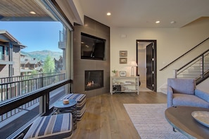 A modern living room with a fireplace, a balcony with outdoor seating, and a view of the mountains. - Juniper Landing 3 Bedroom by Avantstay Condo in Park City Mountain Resort w/ Pool, Hot Tub & Gym (Park City)