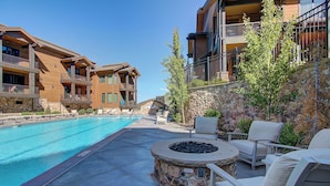 A pool area with lounge chairs, a fire pit, and a stone wall. - Juniper Landing 3 Bedroom by Avantstay Condo in Park City Mountain Resort w/ Pool, Hot Tub & Gym (Park City)
