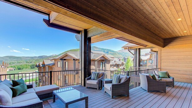 A wooden deck with wicker furniture, a glass table, and a view of houses in the background. - Juniper Landing 3 Bedroom by Avantstay Condo in Park City Mountain Resort w/ Pool, Hot Tub & Gym (Park City)