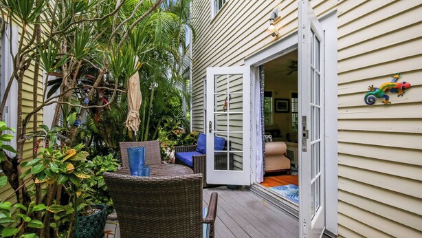 Une terrasse couverte avec des meubles en osier, une porte donnant sur un espace intérieur et une petite décoration représentant un lézard sur le mur.