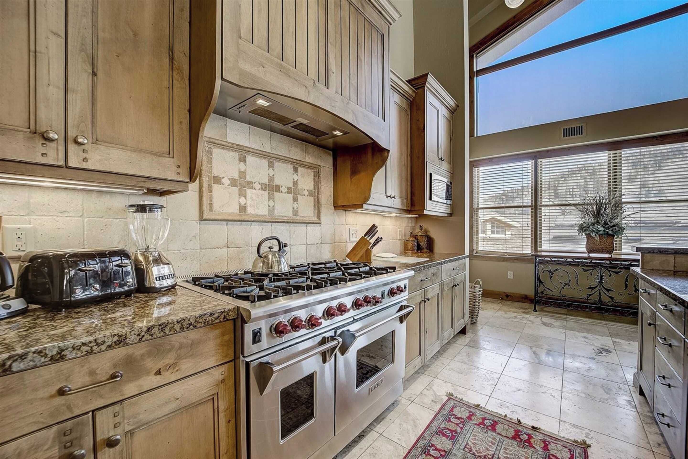 A kitchen with wooden cabinets, a gas stove, a toaster, and a large window with blinds.