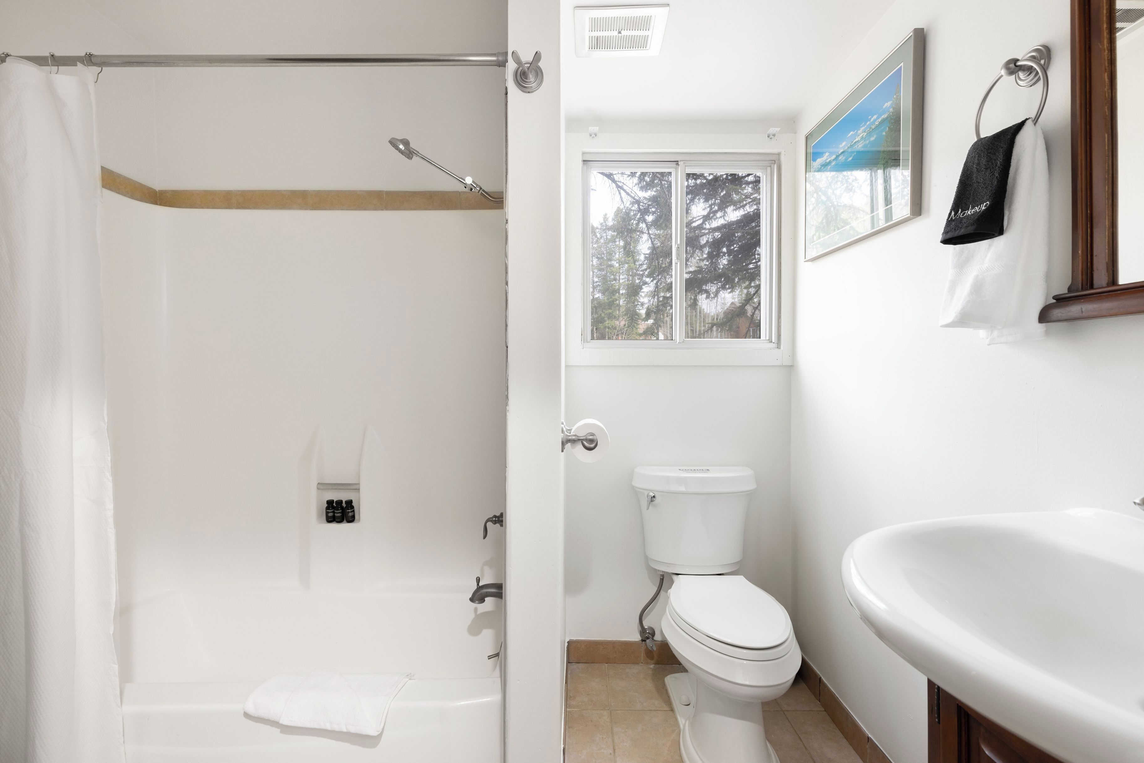 A bathroom with a bathtub, toilet, sink, and a window with a view of trees.