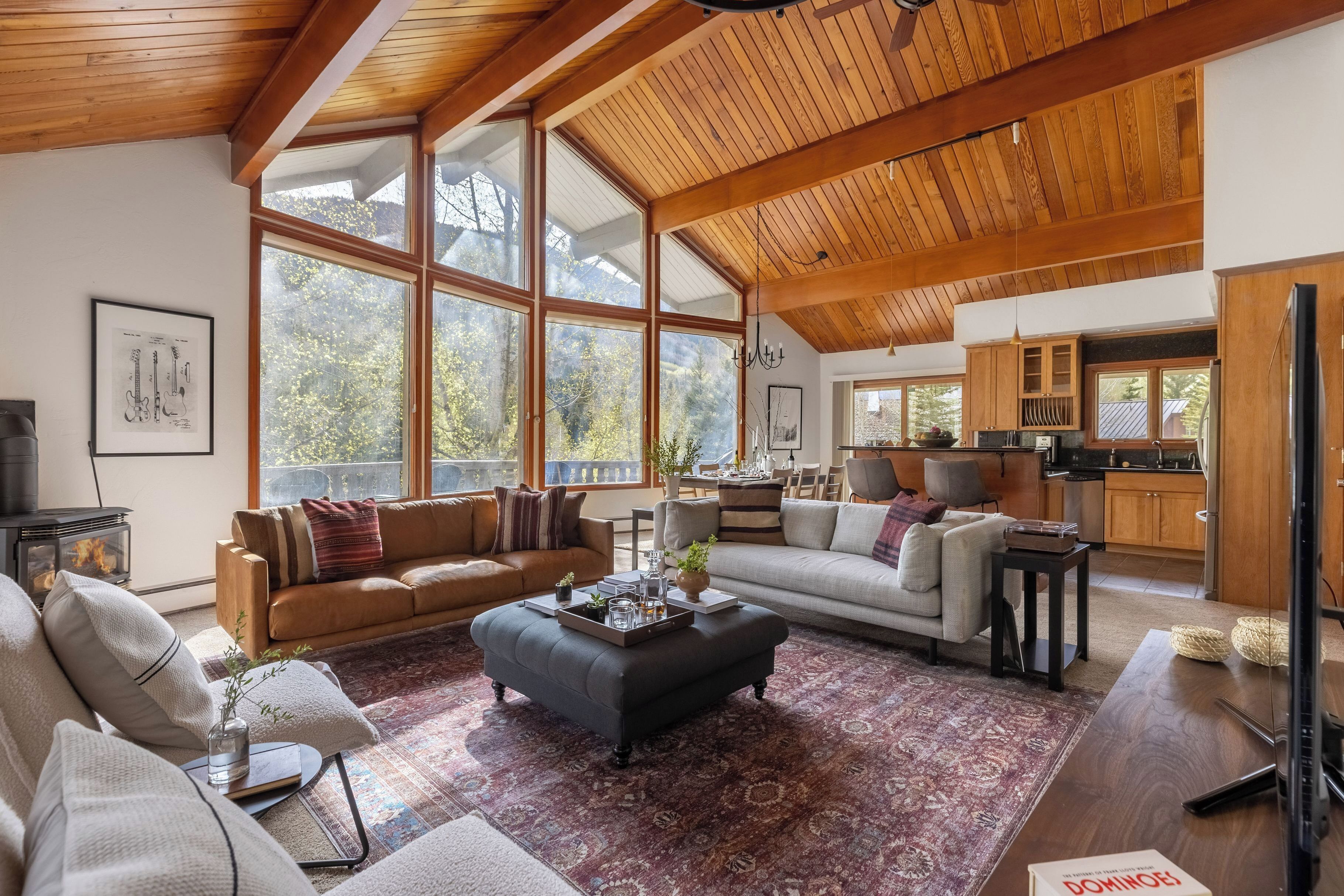 A spacious living area with large windows, a fireplace, and a kitchen in the background.