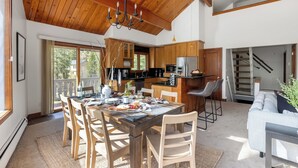 A spacious kitchen with wooden cabinets, a dining area with a table set for four, and a staircase leading to an upper level. - Bighorn by Avantstay Spacious Ski Cabin w/ Sprawling Porch, Views & Hot Tub! (Vail)