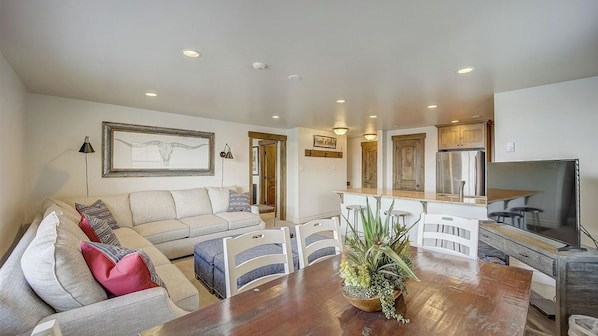 A modern living room with a sofa, dining table, and kitchen area with cabinets and a refrigerator.