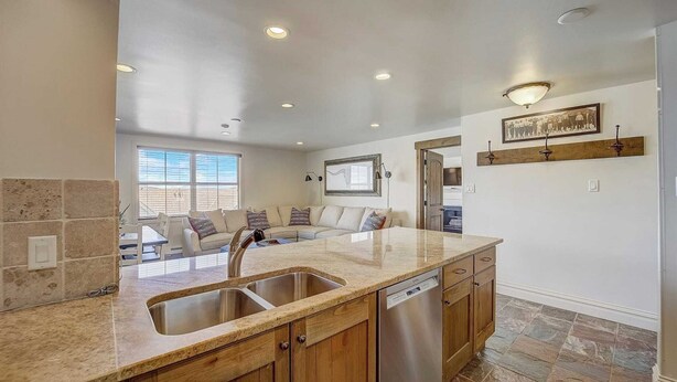 A modern kitchen with a large island, stainless steel sink, wooden cabinets, and a dishwasher. - Resort Plaza #5061 by Avantstay Located in Park City Mountain Resort Close to the Slopes! (Park City)