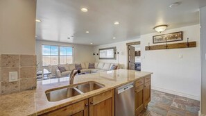 A modern kitchen with a large island, stainless steel sink, wooden cabinets, and a dishwasher. - Resort Plaza #5061 by Avantstay Located in Park City Mountain Resort Close to the Slopes! (Park City)