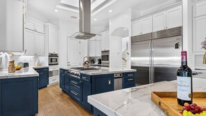 Una cocina moderna con armarios blancos, una isla central, electrodomésticos de acero inoxidable y una botella de vino en la encimera.