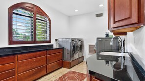Une cuisine équipée d’un lave-linge et d’un sèche-linge intégrés, de meubles en bois, d’un plan de travail noir et d’une fenêtre donnant sur un espace verdoyant.