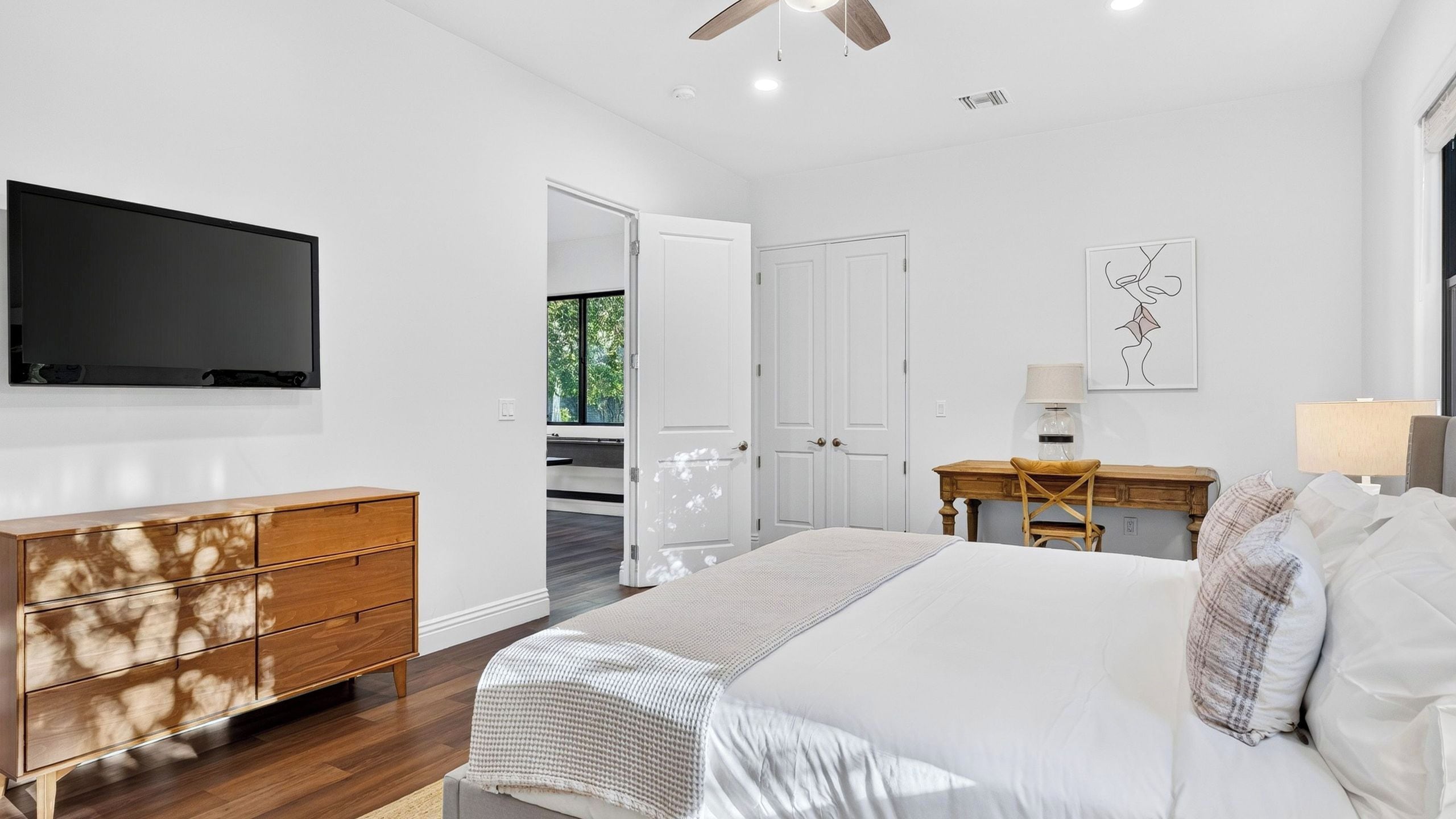 Une chambre moderne avec un grand lit, une commode en bois, un bureau et un téléviseur à écran plat fixé au mur.