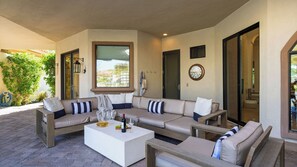 Un espace extérieur aménagé, abrité, avec un ensemble de canapés, une table basse et une bouteille de vin.