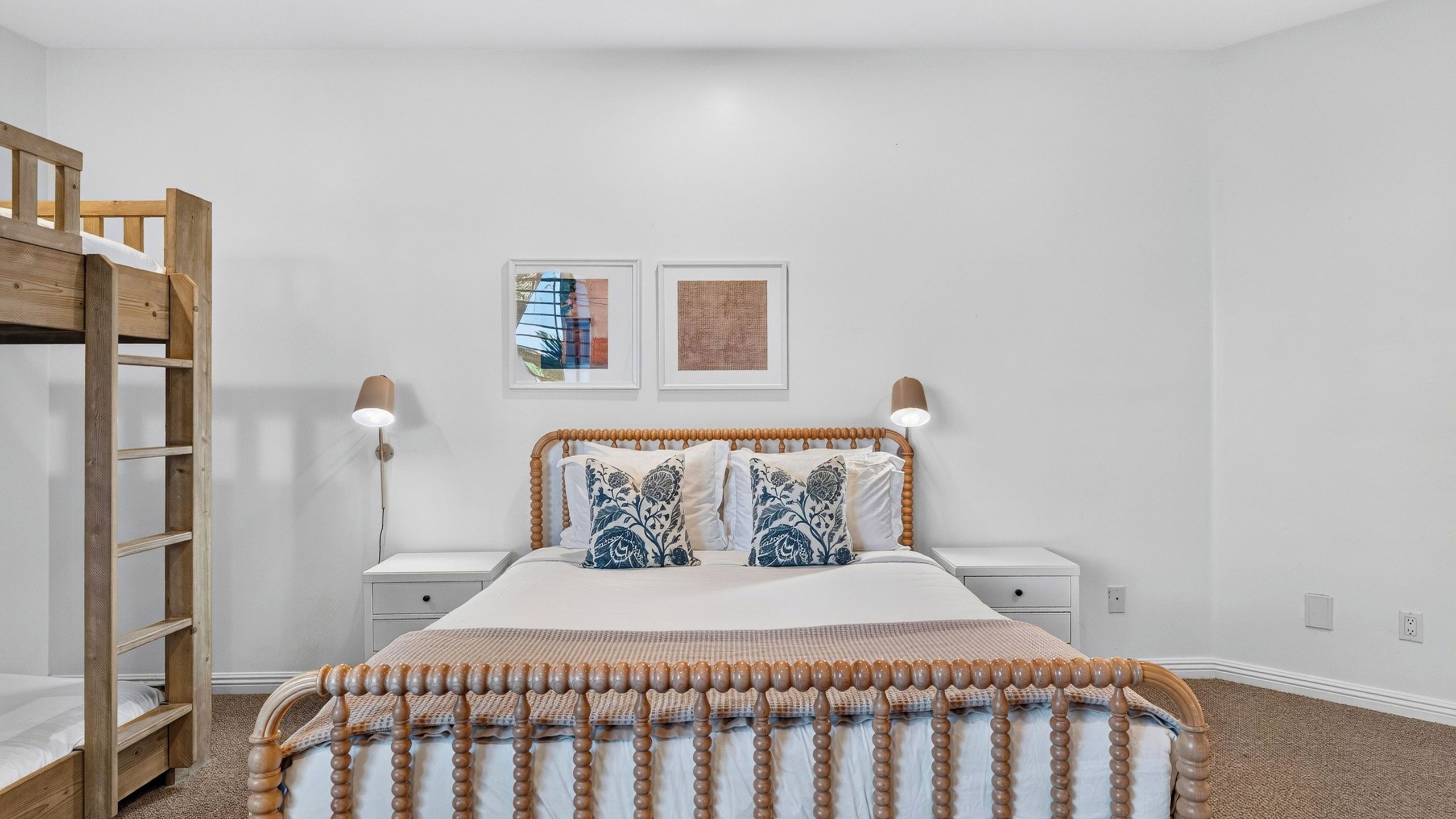 A bedroom with a bunk bed, a bedside table, a lamp, and two framed pictures on the wall.