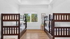 A room with bunk beds, a window with a view of greenery, and a small table with a plant. - Villa Verbena by Avantstay Expansive Estate w/ B-ball Court, Pool/spa & Entertainer's Yard (Indio)
