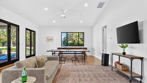 Un salon moderne comprenant un canapé, une table basse, un téléviseur et une grande fenêtre donnant sur un paysage verdoyant.