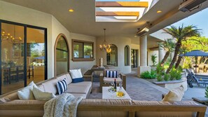 Eine Außenpatio-Terrasse mit einer Couch, einem Esstisch und Stühlen, umgeben von Pflanzen und einer Pergola.