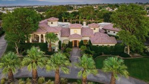 A large, multi-story house with a tiled roof, surrounded by palm trees and a well-maintained lawn. - Villa Verbena by Avantstay Expansive Estate w/ B-ball Court, Pool/spa & Entertainer's Yard (Indio)