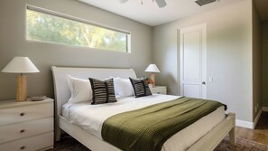 A bedroom with a bed, two bedside tables, a window, and a door. - Villa Verbena by Avantstay Expansive Estate w/ B-ball Court, Pool/spa & Entertainer's Yard (Indio)