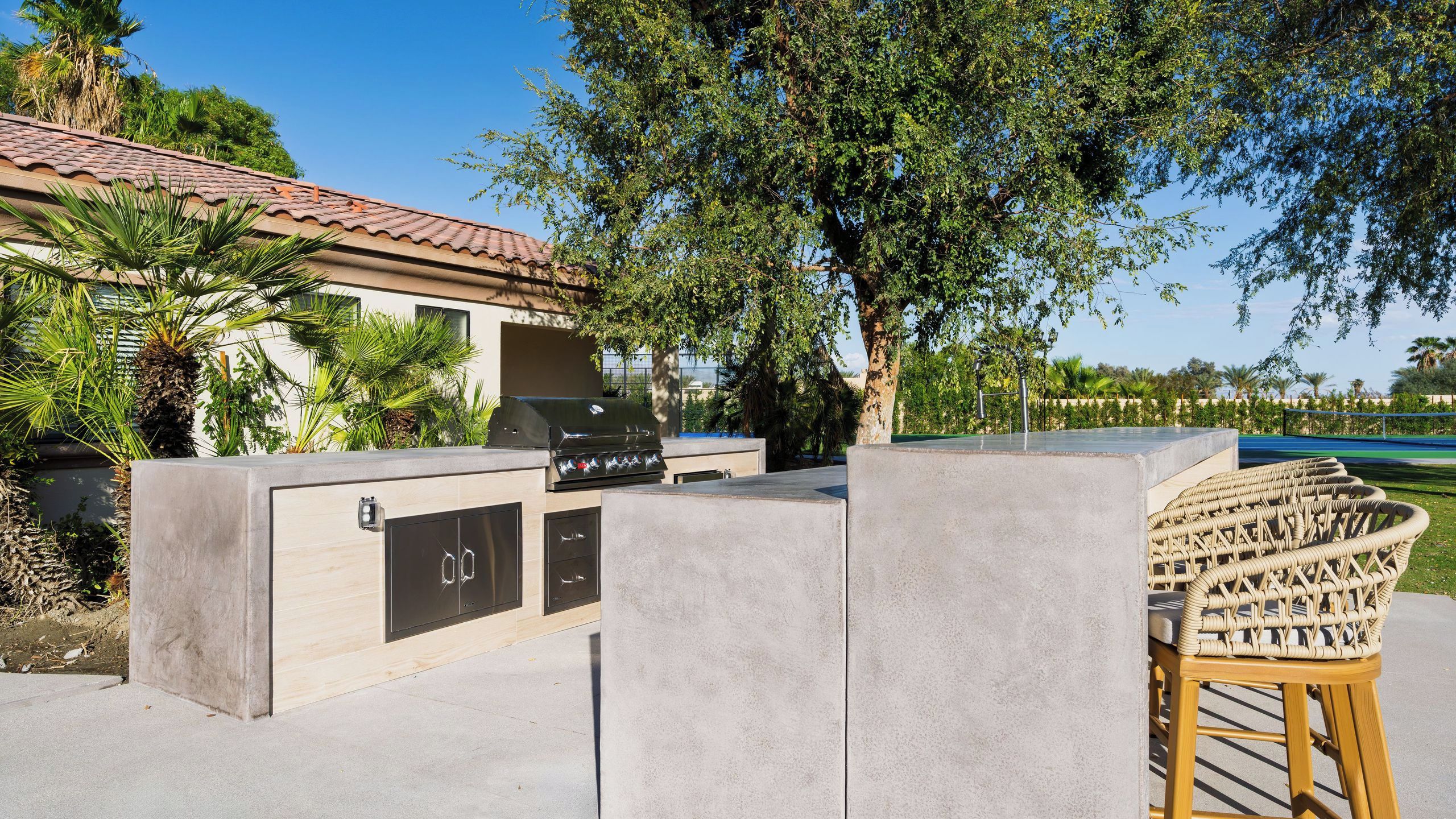 Un patio con una parrilla, una zona de estar de hormigón y una piscina al fondo.