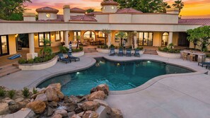 A pool area with lounge chairs, a swimming pool, and a building with multiple windows and a tiled roof. - Villa Verbena by Avantstay Expansive Estate w/ B-ball Court, Pool/spa & Entertainer's Yard (Indio)
