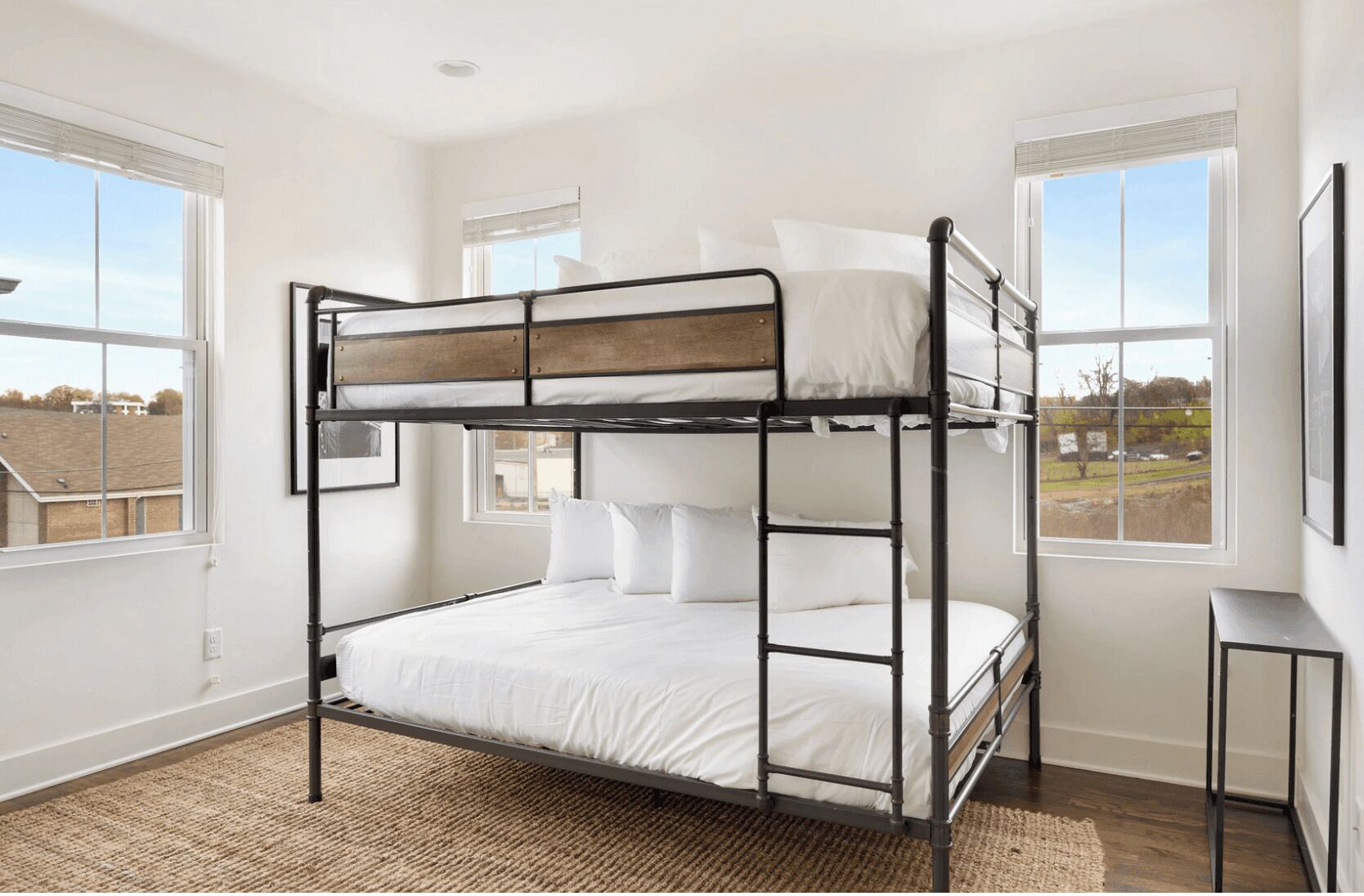 A bunk bed in a room with large windows, a wooden floor, and a small table.