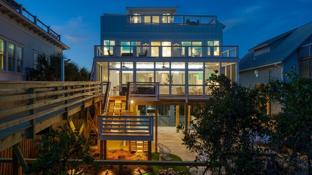 Una moderna casa a più piani con un balcone, posti a sedere all'aperto e un patio in legno.
