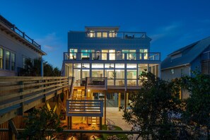 A modern multi-story house with a balcony, outdoor seating, and a wooden deck. - Ocean's Eye by Avantstay Beach Front Home w/ Roof Top, Pool & Putting Green! (Folly Beach)