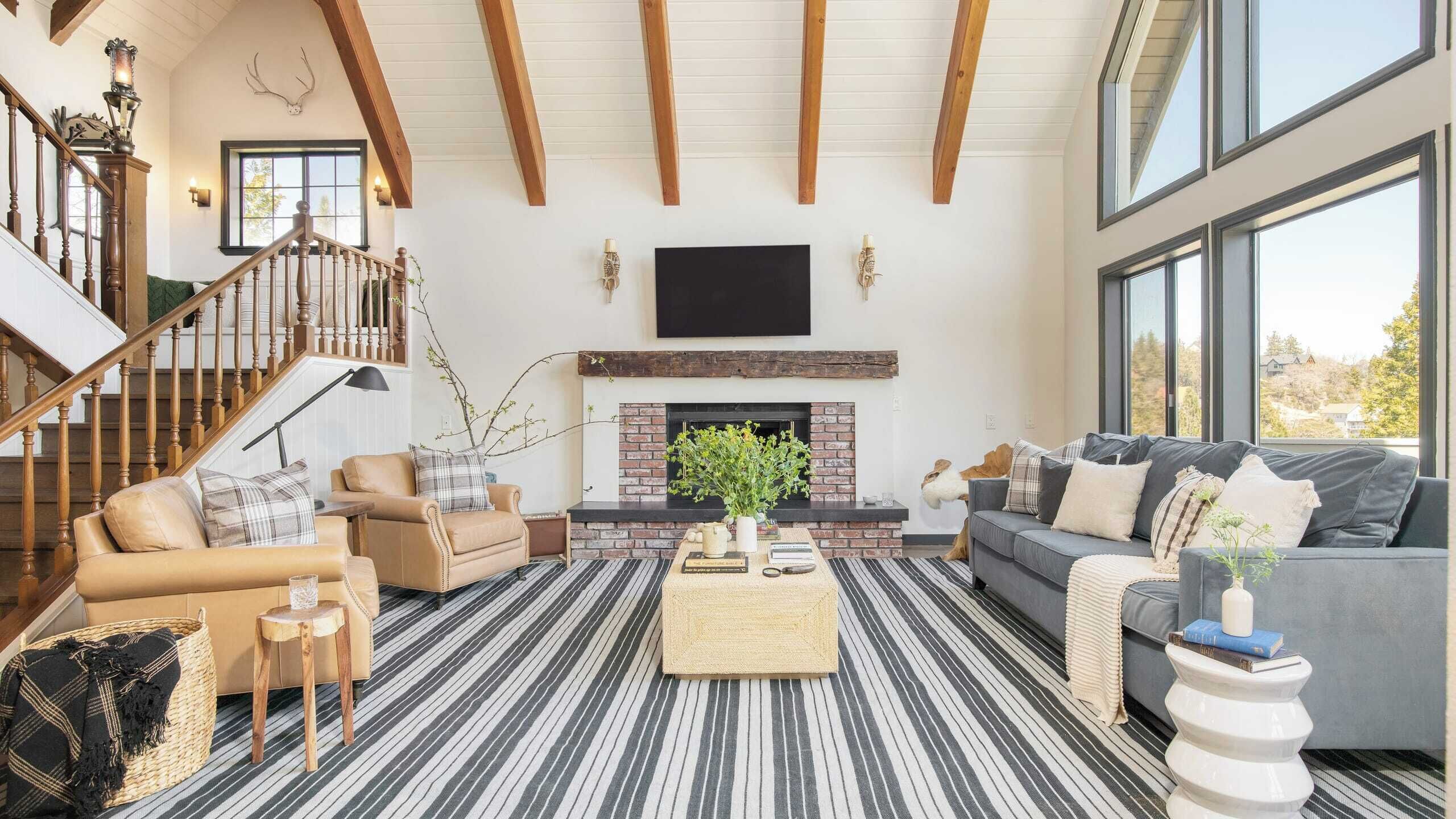 Amplia sala de estar con chimenea, una escalera y ventanas grandes.