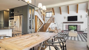 Un vaste espace de vie comprenant une table à manger en bois, une cheminée et un escalier menant à un niveau supérieur.
