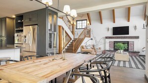 Ein großzügiger Wohnbereich mit Esstisch aus Holz, Kamin und Treppe, die in eine obere Ebene führt.