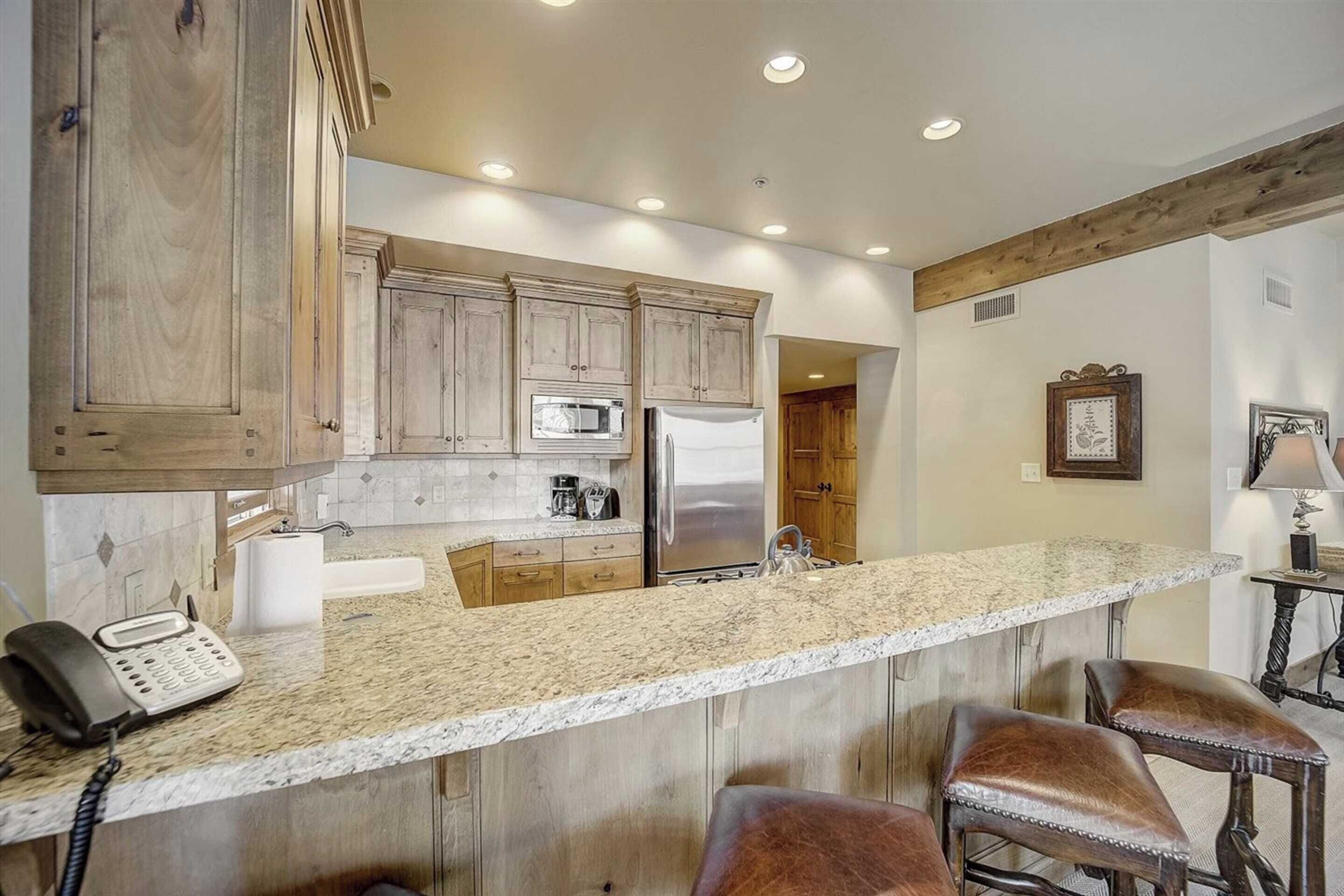 A kitchen with wooden cabinets, a granite countertop, stainless steel appliances, and a telephone.