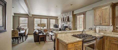 A spacious kitchen with a large island, wooden cabinets, and a stone fireplace.